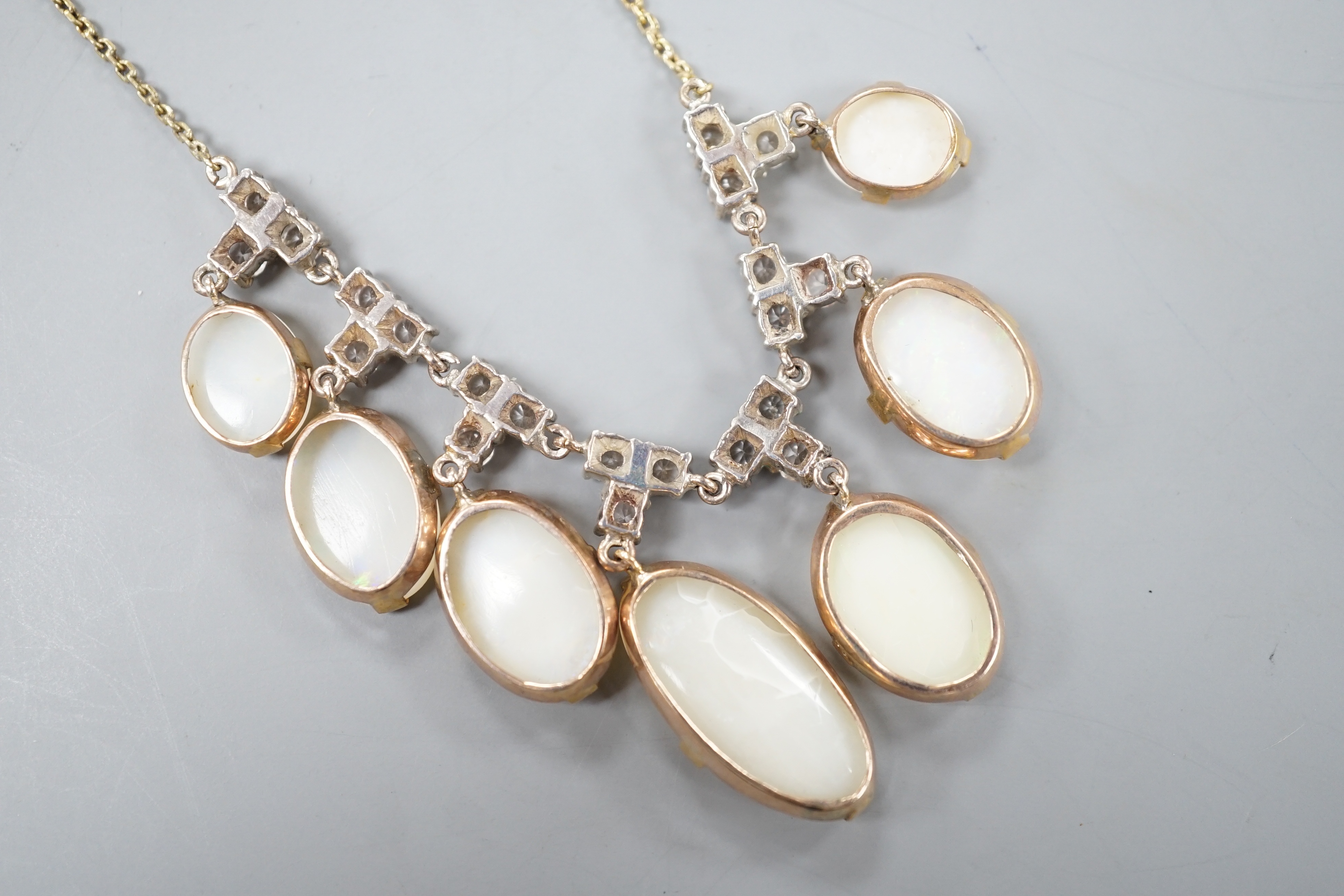 A yellow metal, graduated seven stone oval white opal and paste set cluster fringe necklace, 42cm, gross 14.6 grams.